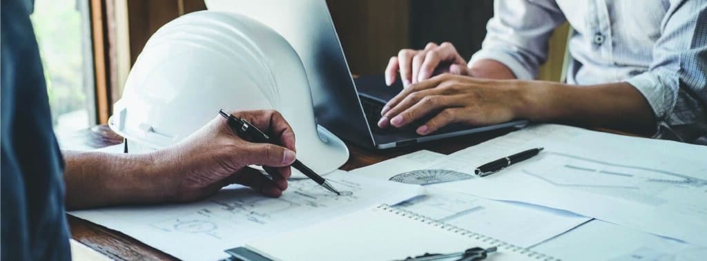 Engineers reviewing plans on paper and on a laptop.