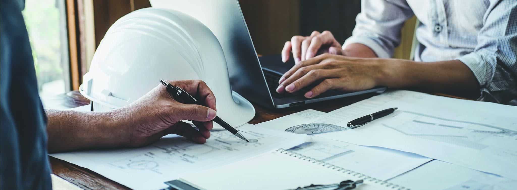 Engineers reviewing plans on paper and on a laptop.