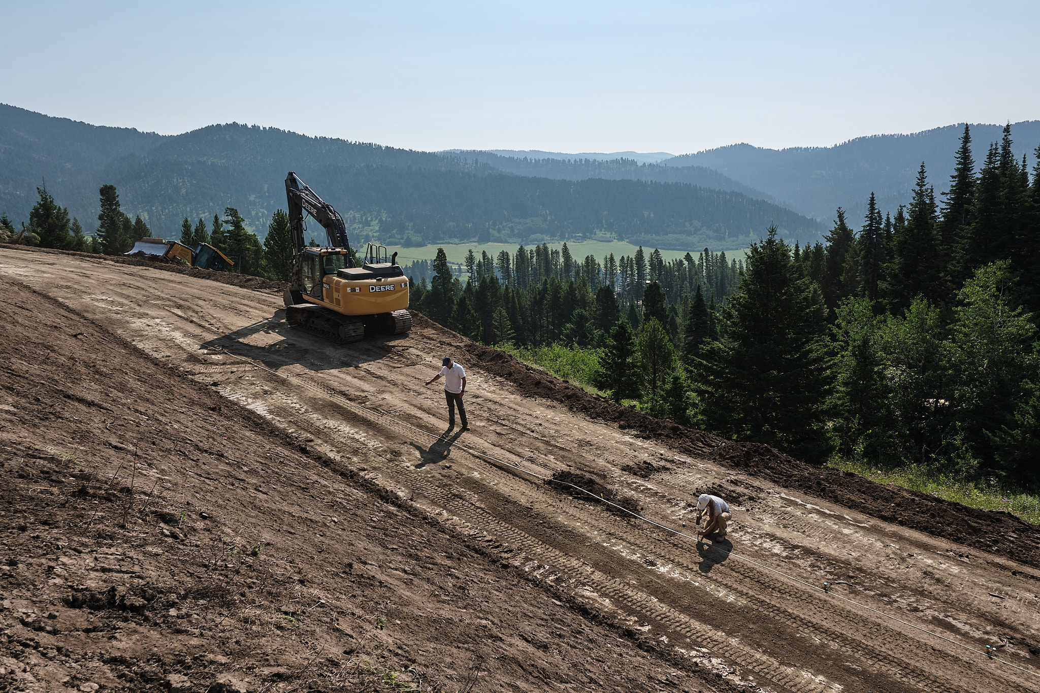 Geotechnical engineers setting up equipment at a project in the Bridger Canyon with mountains in the background.