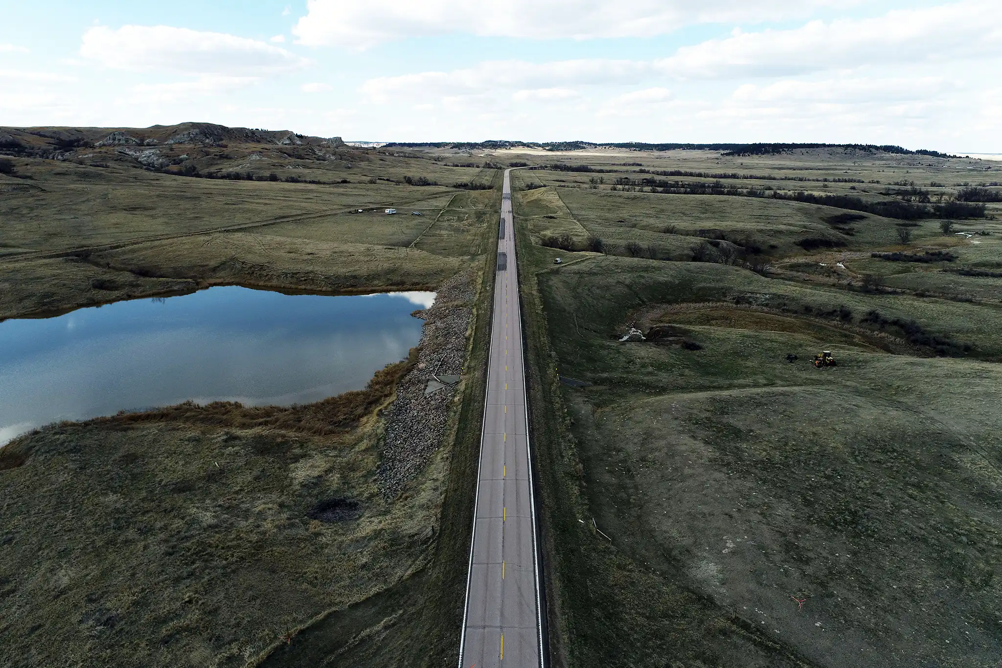 aerial view of Rabbit Creek Dam inspection and hazard analysis, featuring a pond, a road, and the Montana plains.